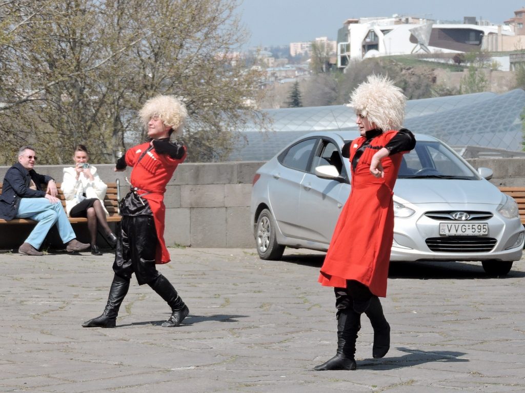 zwei Tänzer mit Fellmützen tanzen auf einem Platz in Tiflis