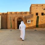 Araber in weißer Kleidung geht auf ein altes arabisches Haus zu, Emirat Sharjah