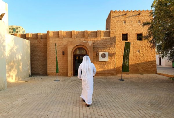 Araber in weißer Kleidung geht auf ein altes arabisches Haus zu, Emirat Sharjah