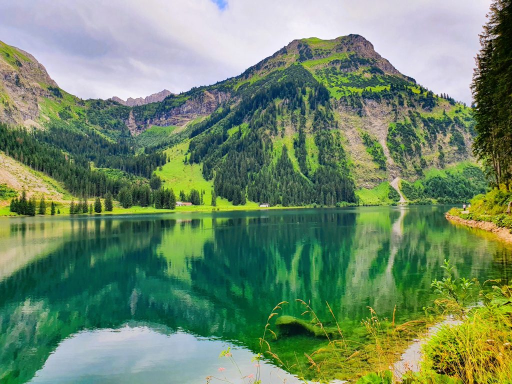 grüner Bergsee in dem sich die hohen Berge spiegeln