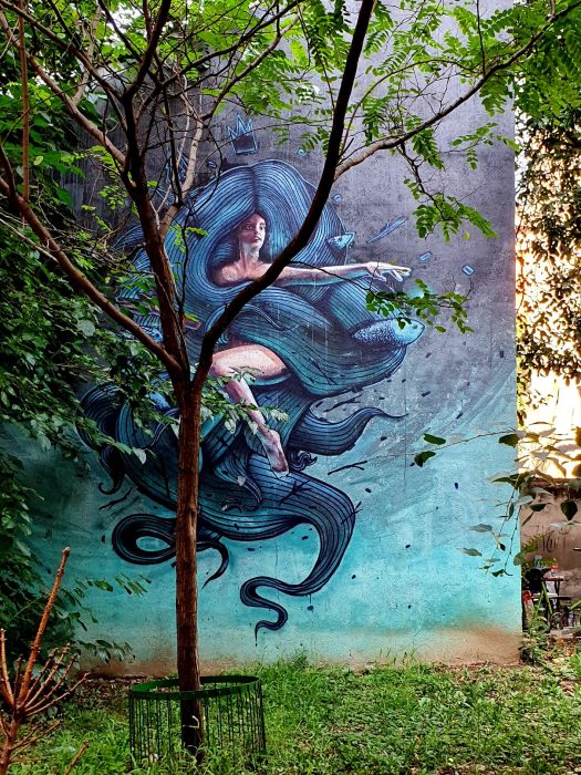 blaufarbiges Mural hinter einem Baum