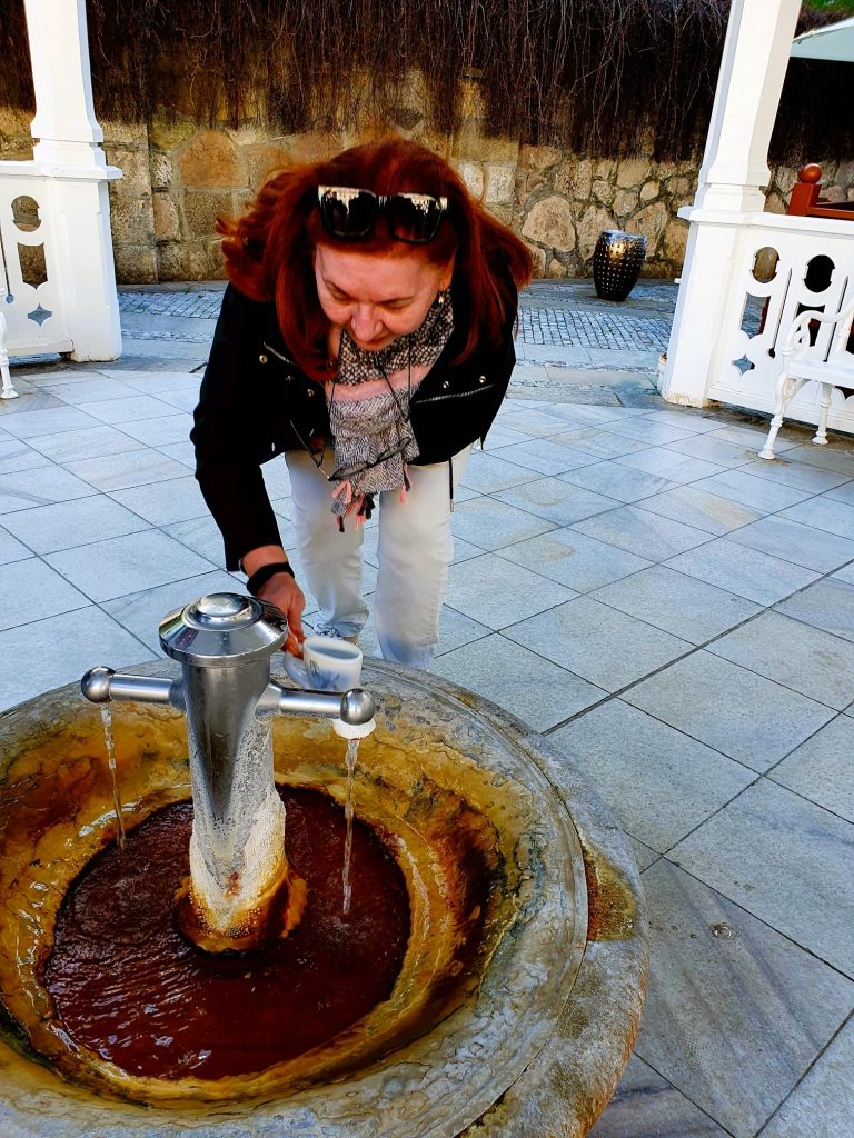 Frau entnimmt Heilwasser aus einem Brunnen
