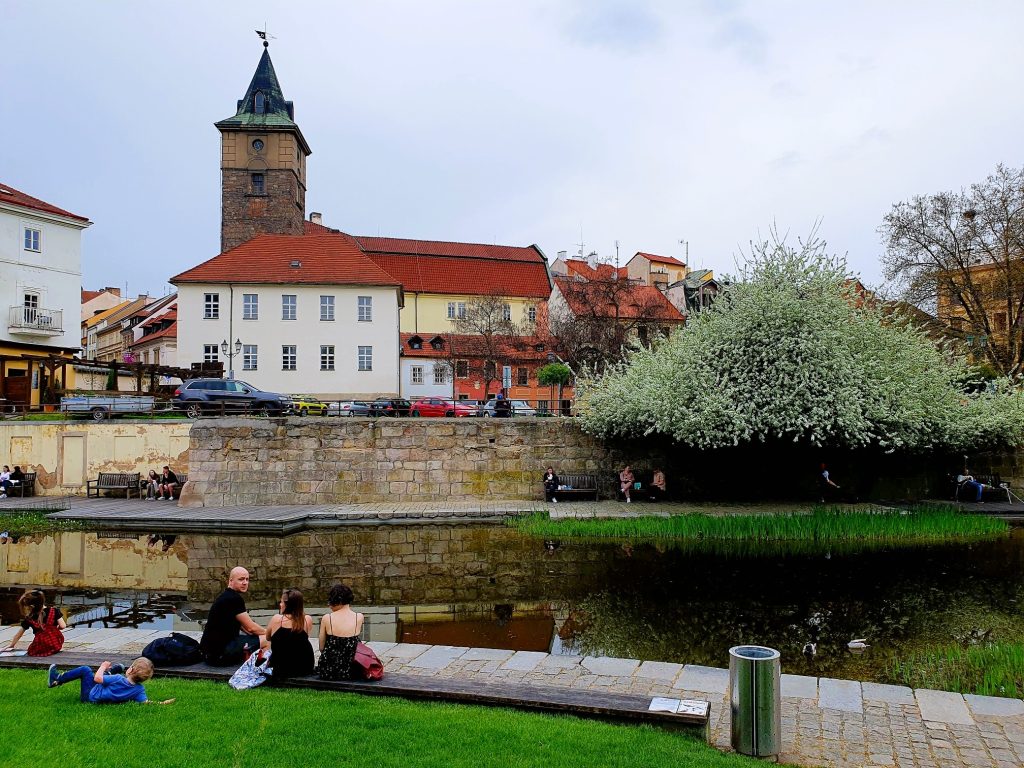 Menschen sitzen am Flussufer mit Blick auf alte Gebäude, Pilsen Altstadt