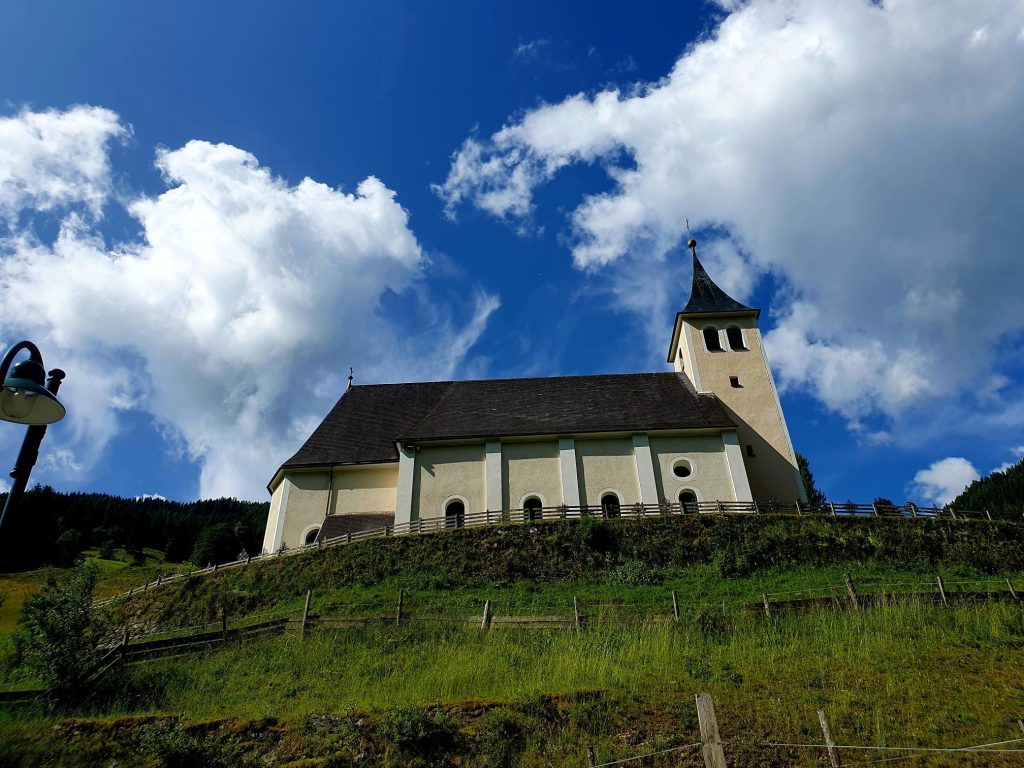 Pfarrkirche auf einem grünen Berghügel, Hüttschlag