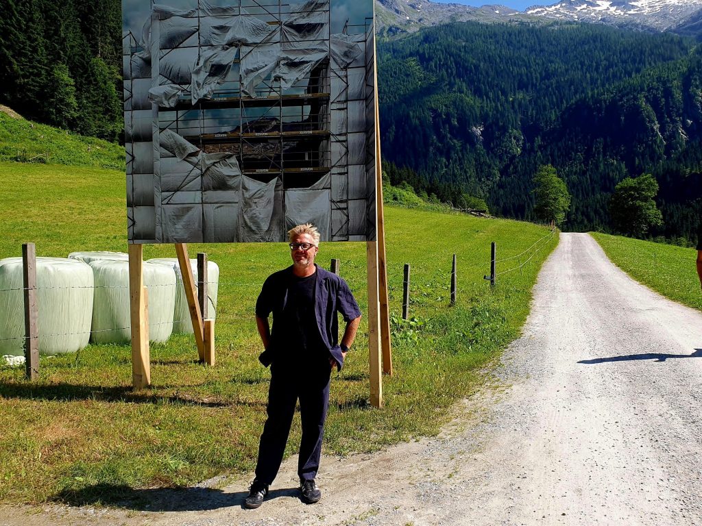 Fotokünstler steht vor seinem Fotoprojekt, einer Tafel in der Landschaft, Kunstroas Hüttschlag