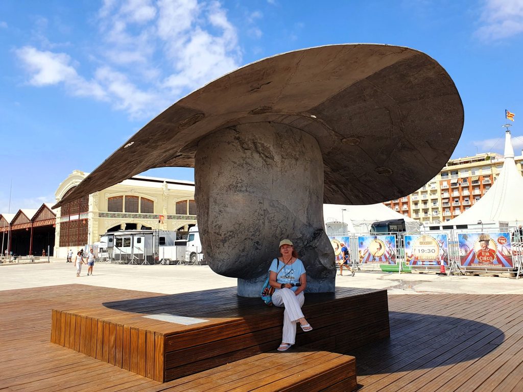 Frau unter dem Schatten einer großen Hut-Skulptur sitzend