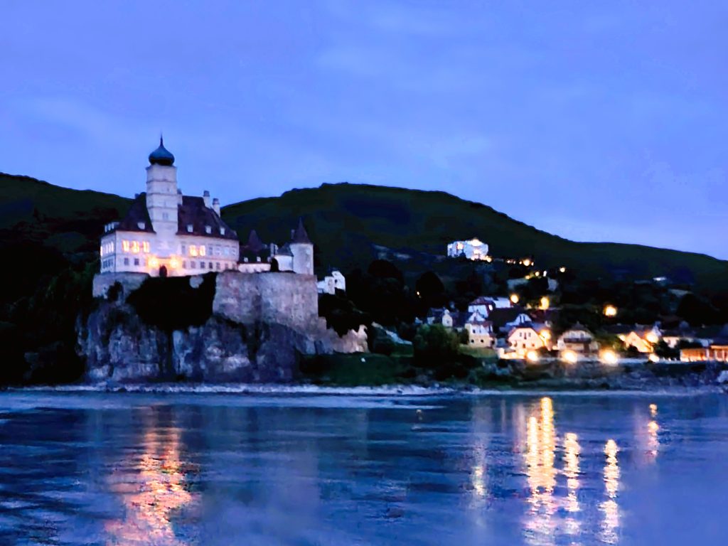Schloss mit Turm auf Hügel und Flusslandschaft bei Nacht