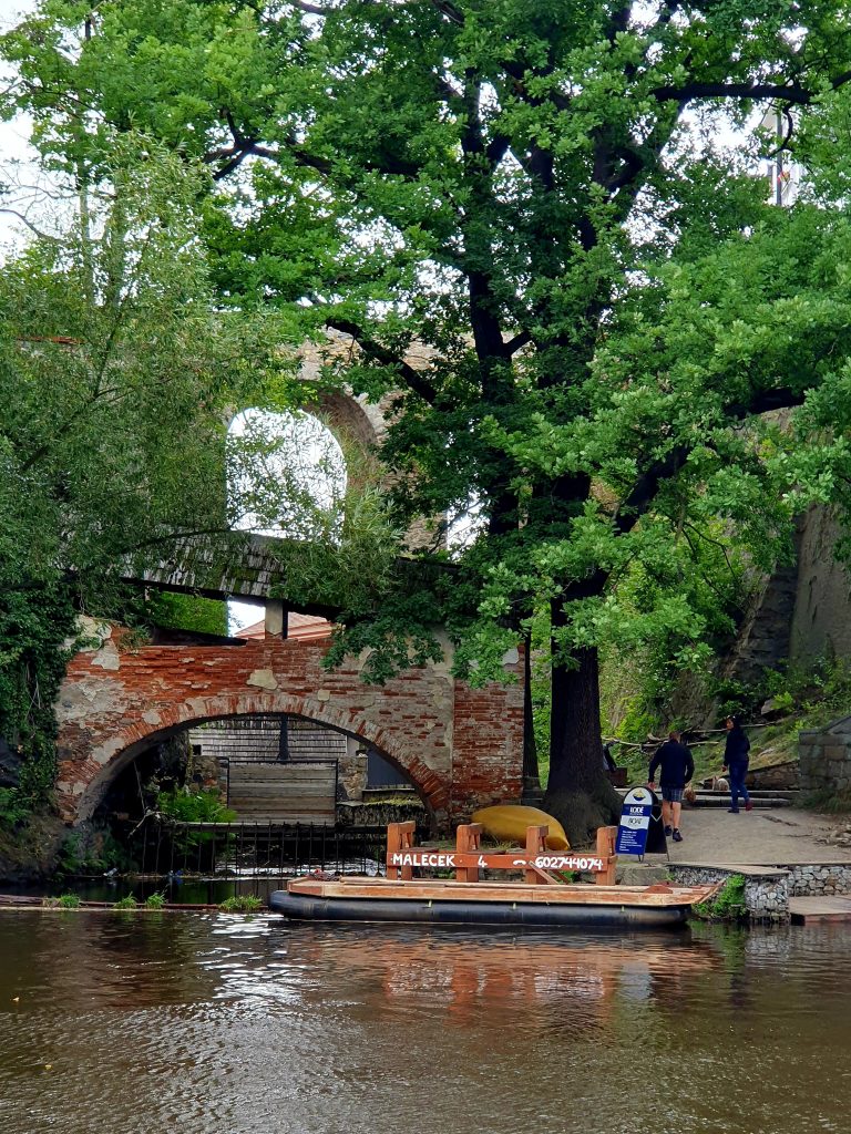 Bootsanlegestelle am Fluss mit alter Steinbrücke, Krumau Floßfahrt