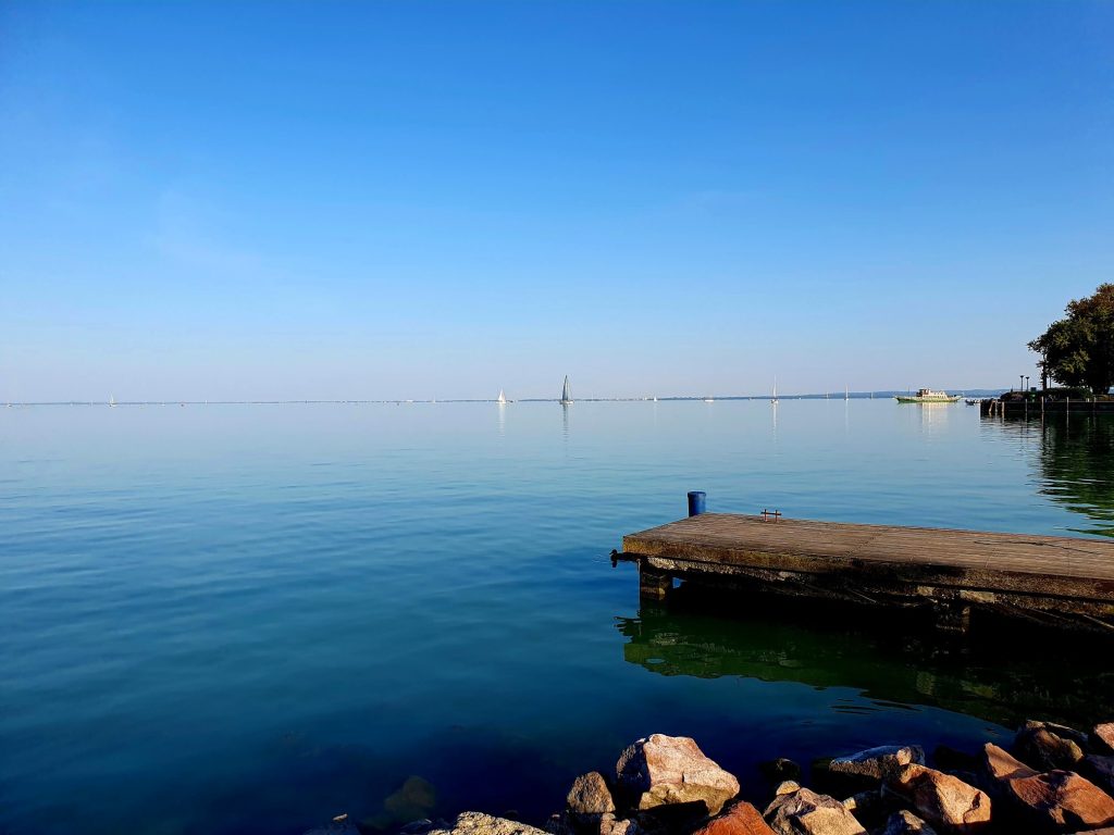 Blick auf den ruhigen, blauen See in den ein Steg führt