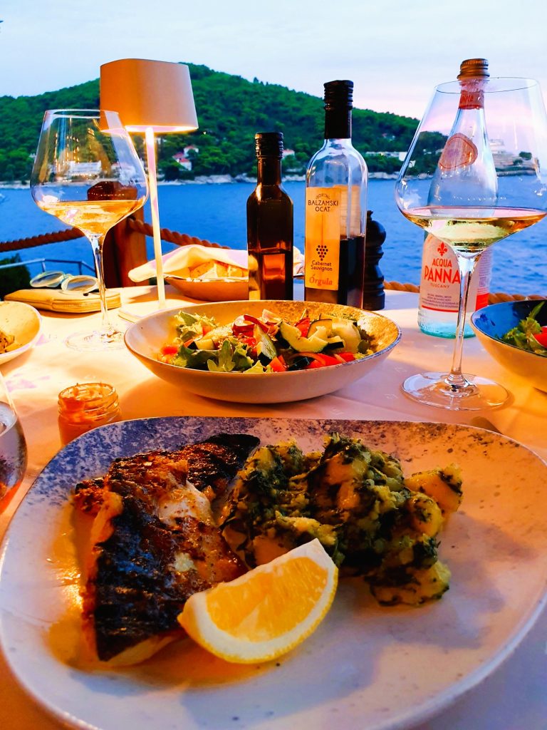 mediterranes Fischgericht mit Salat und Gläser auf einem Restauranttisch