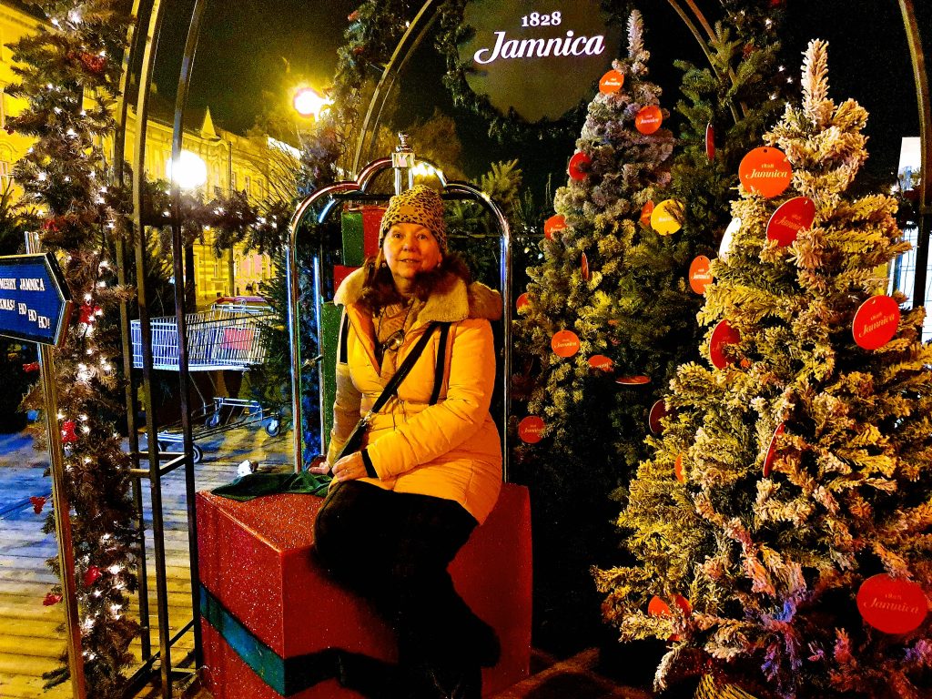 Reisebloggerin sitzt zwischen nächtlich beleuchteten Weihnachtsbäumen