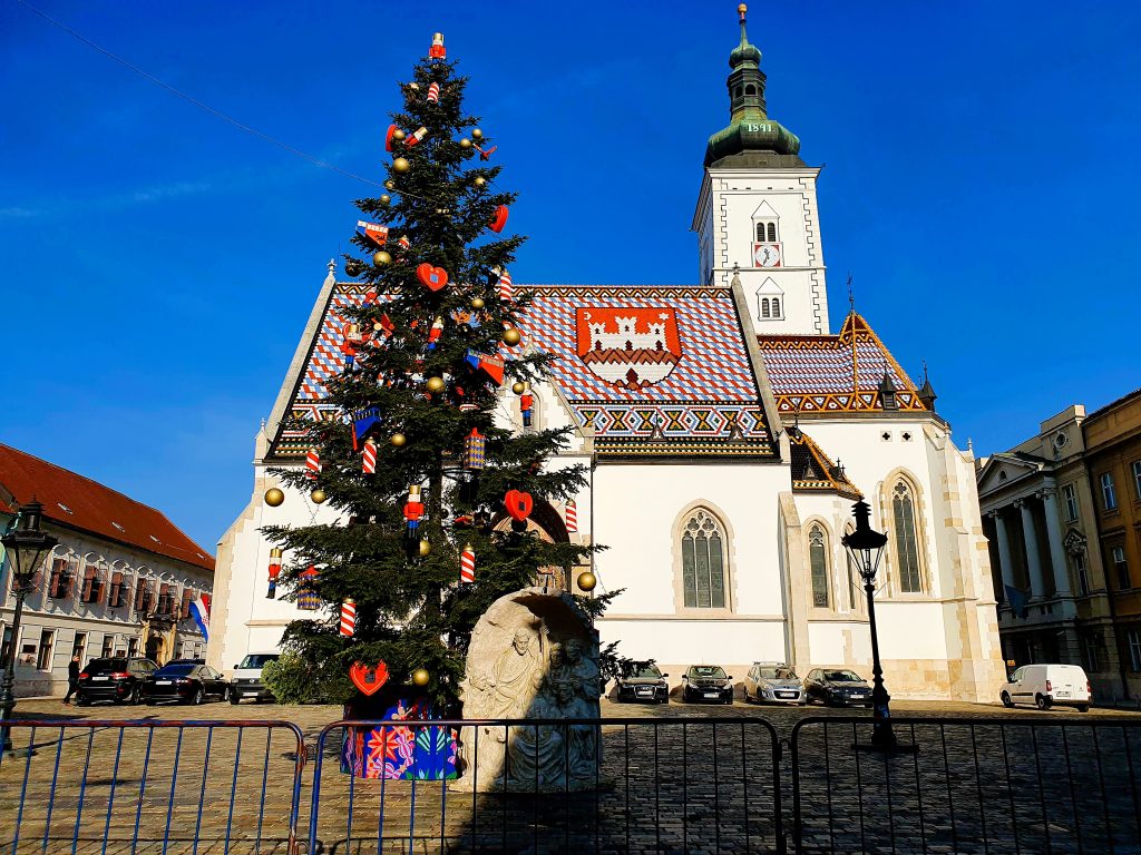 Kirche mit Dach, das von kroatischen Wappen geziert ist, davor Weihnachtsbaum, Zagreb Sehenswürdigkeit