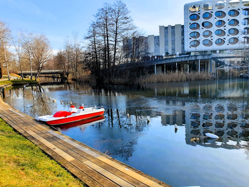ein Kanal mit Boot und am Ufer ein Hotel, Seepark Hotel Klagenfurt