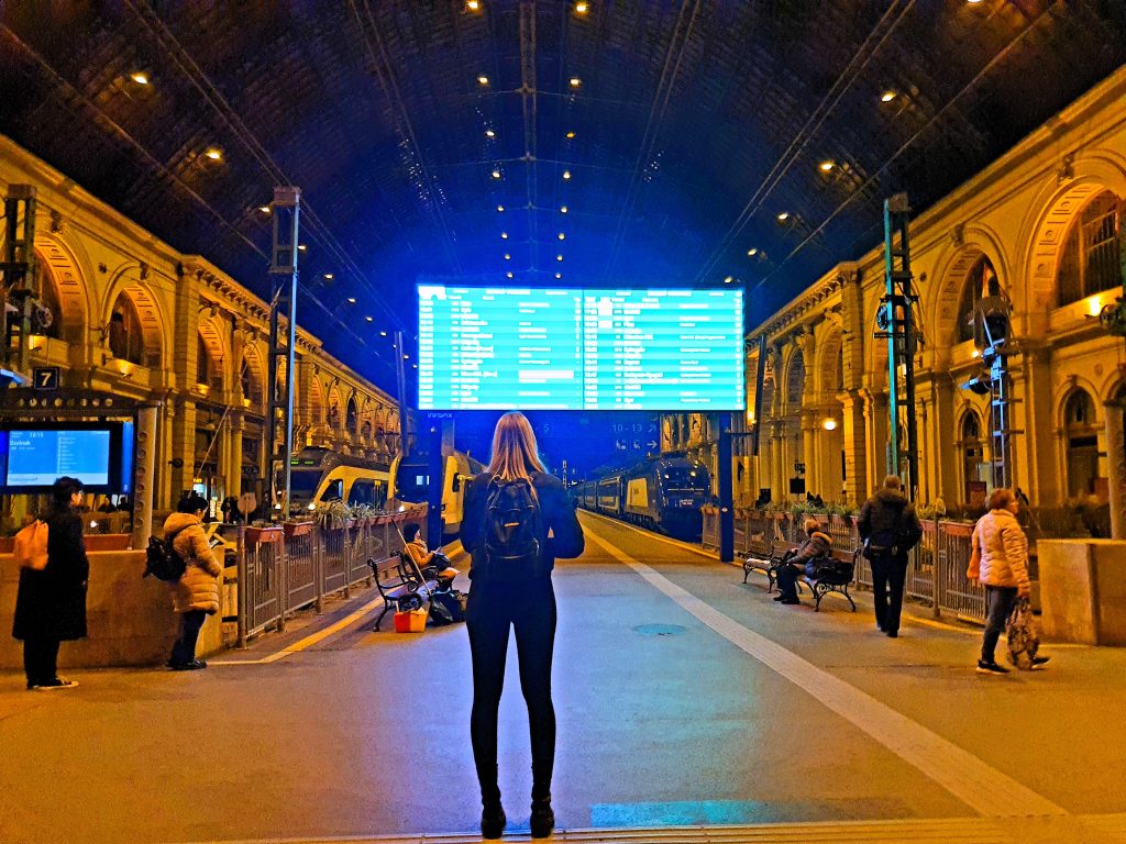 Frau steht vor Zug-Abfahrt-Display Bahnhof Budapest Keleti Pu.