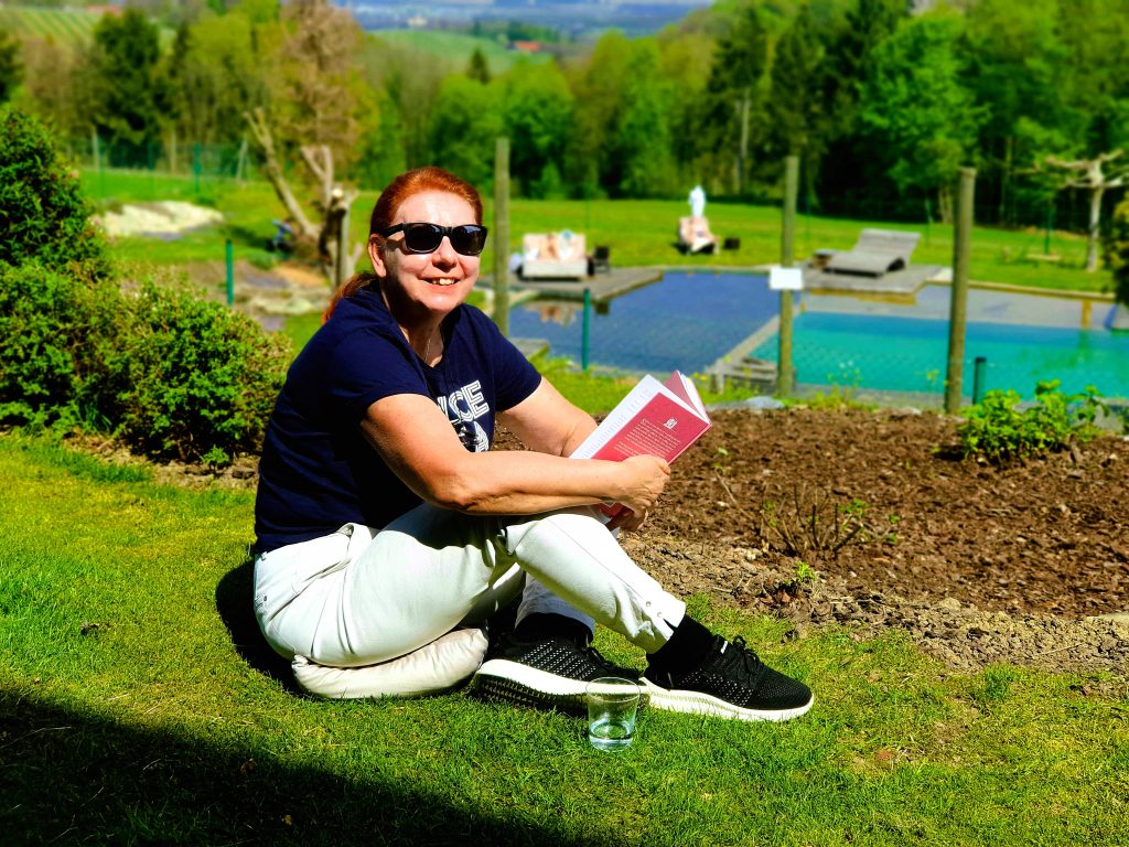 Bloggerin mit Sonnenbrille sitzt im Gras und liest ein Buch