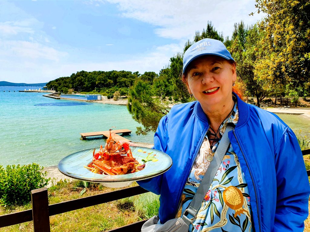 Frau hält einen Teller mit mediterranem Seafood Gericht in der Hand, Blick aufs Meer, Kroatien