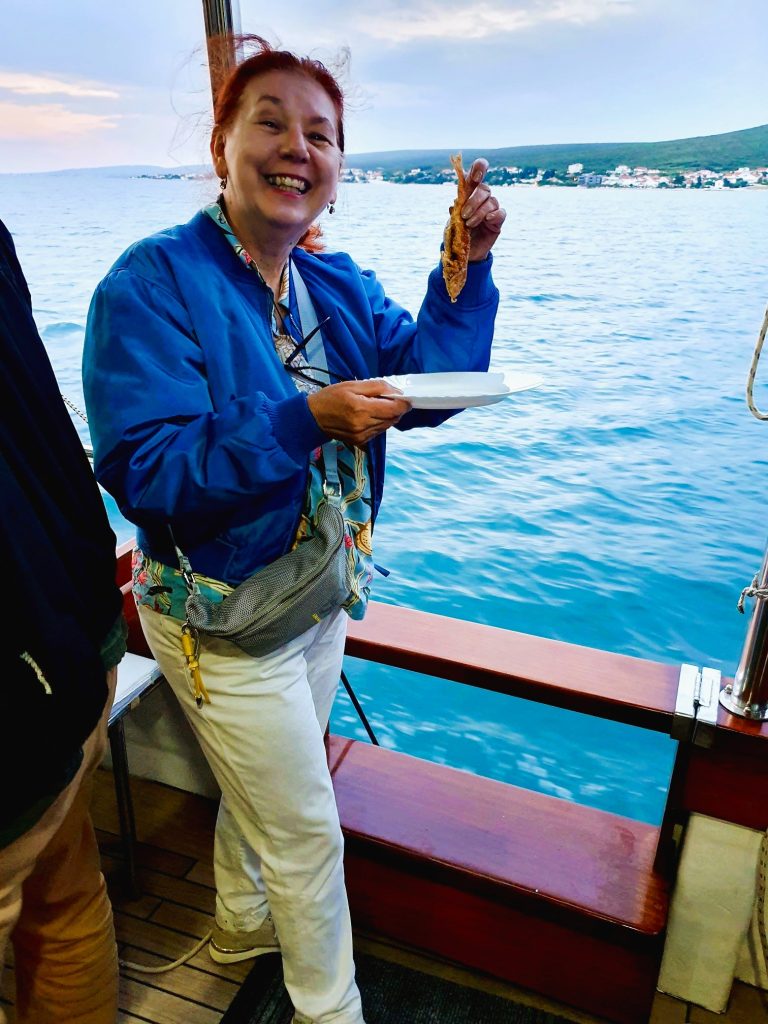 Frau steht auf einem Boot und hält einen gebratenen Fisch in der Hand