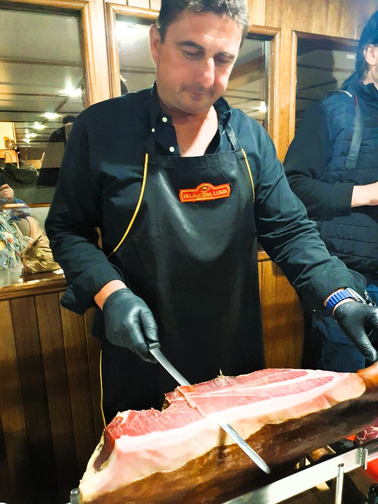 Mann schneidet fachmännisch mit Messer einen dalmatinischen Schinken; Genuss-Reise Kroatien