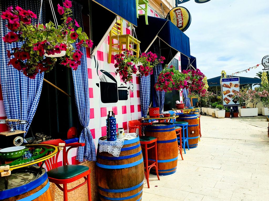Häuserzeile mit Lokal in den kroatischen Farben weiß-rot-blau mit Holzfässern und Blumendekoration